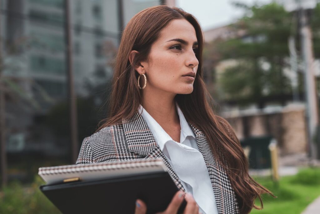 Portrait of a confident businesswoman outdoors in formal attire, holding a notebook and exuding professionalism.