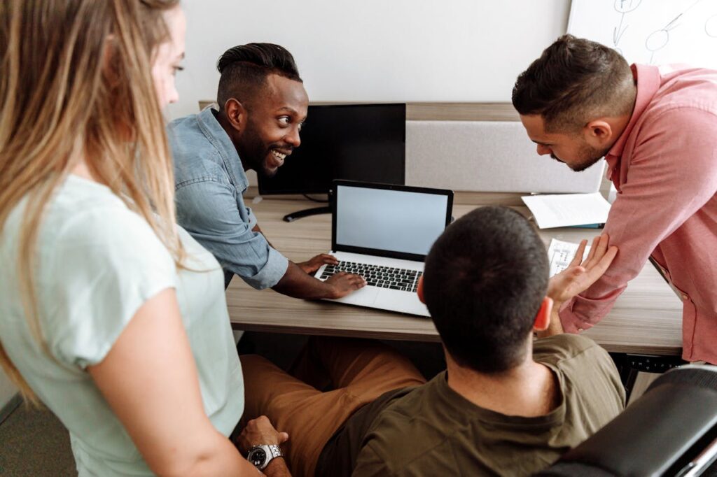 Four colleagues brainstorming around a laptop in a bright, modern office setting.